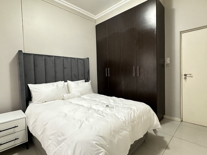 A well-maintained bedroom featuring dark wood built-in cupboards, neutral tiled flooring, and classic cornice detailing.