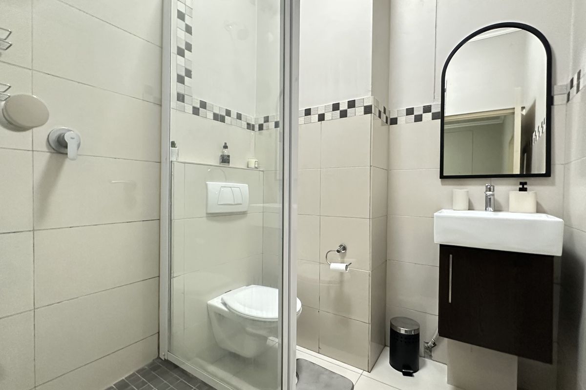 A compact, modern bathroom featuring a wall-mounted toilet, glass-enclosed shower, and a vanity unit with a basin and mirror.