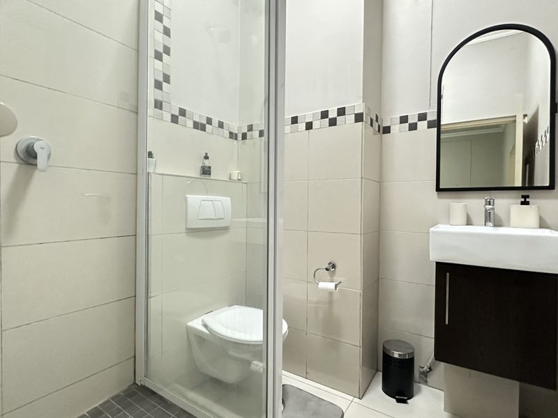A compact, modern bathroom featuring a wall-mounted toilet, glass-enclosed shower, and a vanity unit with a basin and mirror.