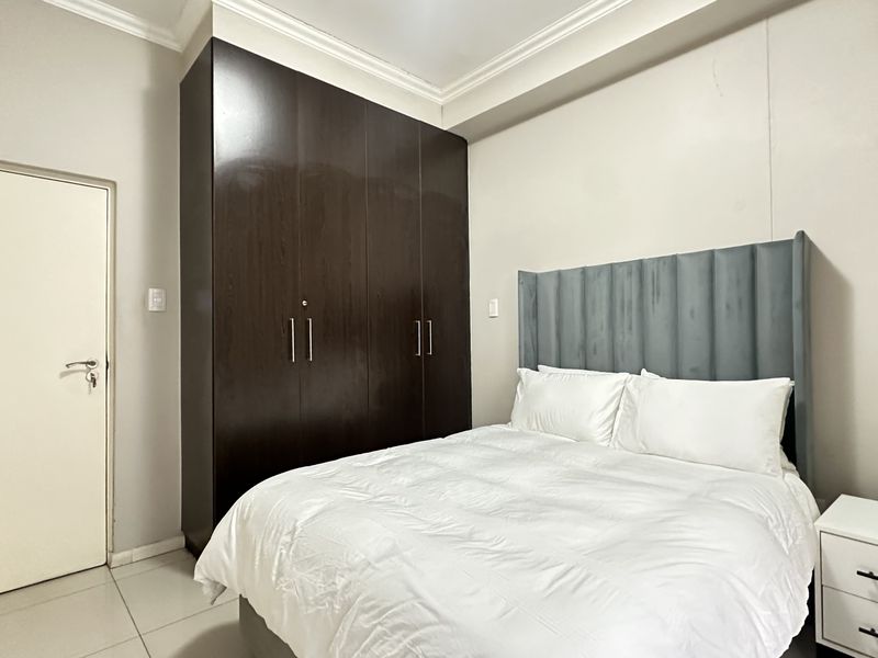 A well-maintained bedroom featuring a large dark wood built-in wardrobe, crown molding, and tiled flooring, providing a clean and functional living space.