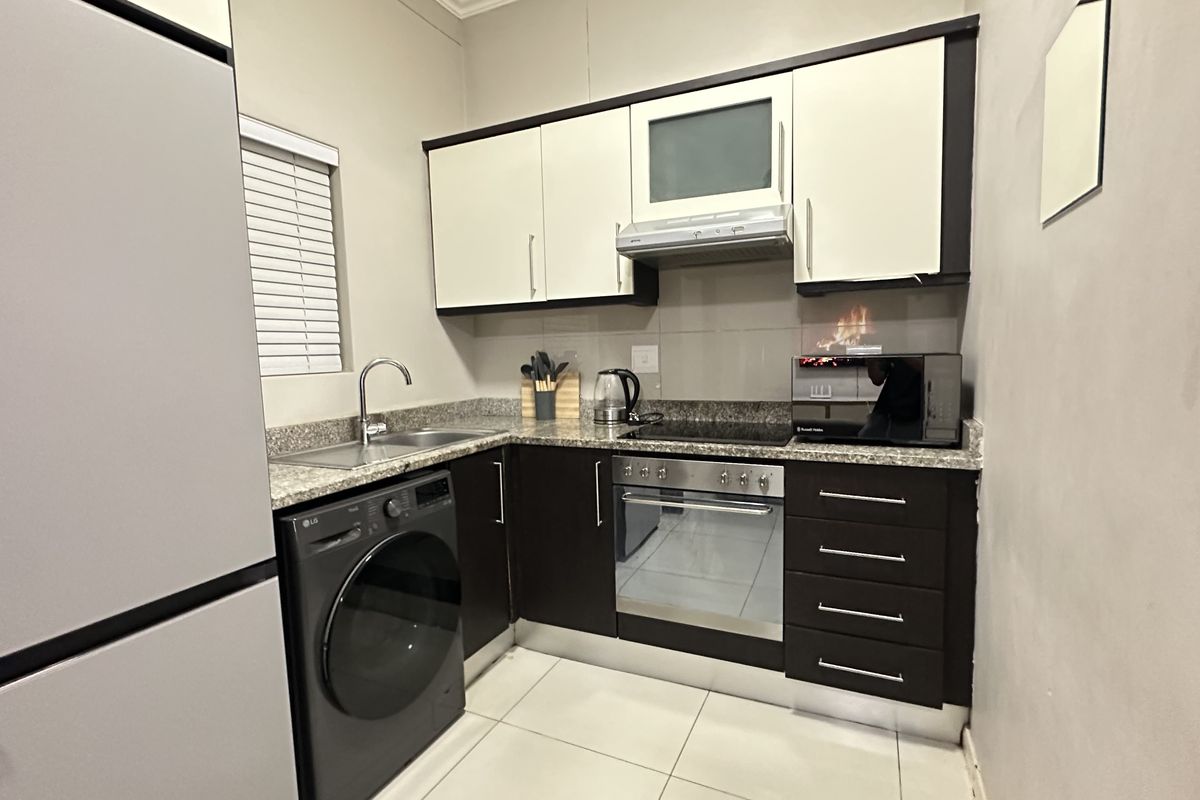 Compact modern kitchen featuring dark cabinetry, granite countertops, integrated oven and hob, and tiled flooring with a functional layout.