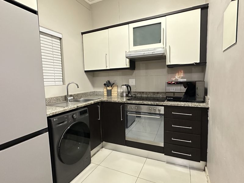 Compact modern kitchen featuring dark cabinetry, granite countertops, integrated oven and hob, and tiled flooring with a functional layout.