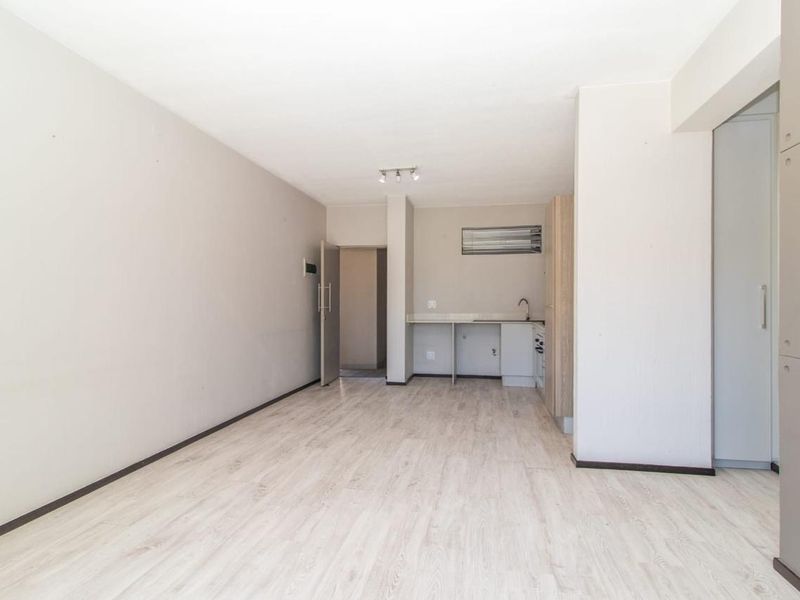 An open-plan living area featuring light laminate flooring and a compact kitchenette with built-in cabinetry and a sink.