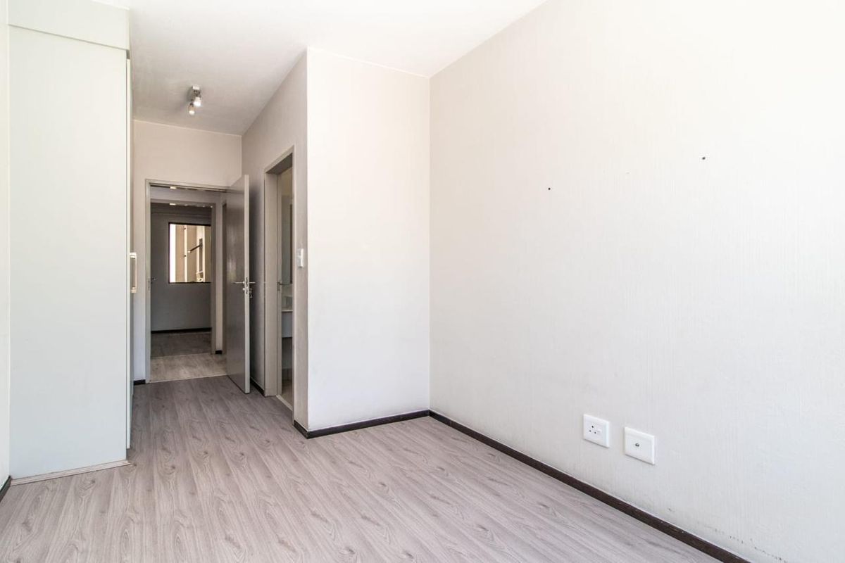 A bright, empty bedroom featuring modern laminate flooring, a built-in wardrobe, and neutral wall finishes, providing a clean canvas for personalization.