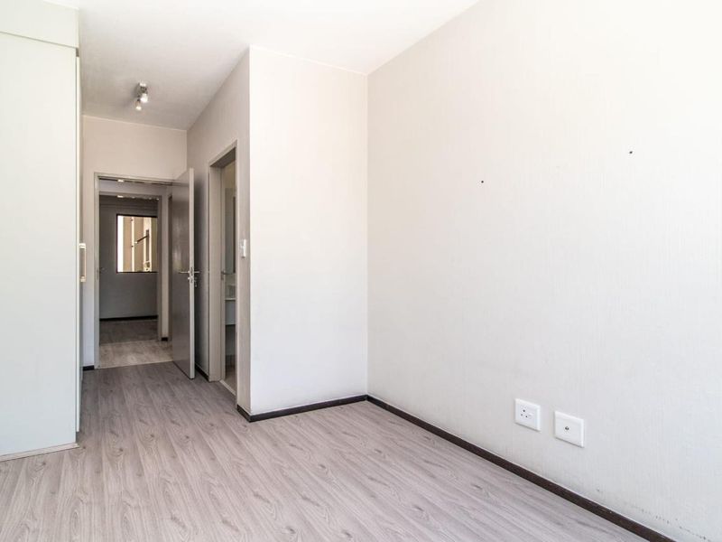 A bright, empty bedroom featuring modern laminate flooring, a built-in wardrobe, and neutral wall finishes, providing a clean canvas for personalization.