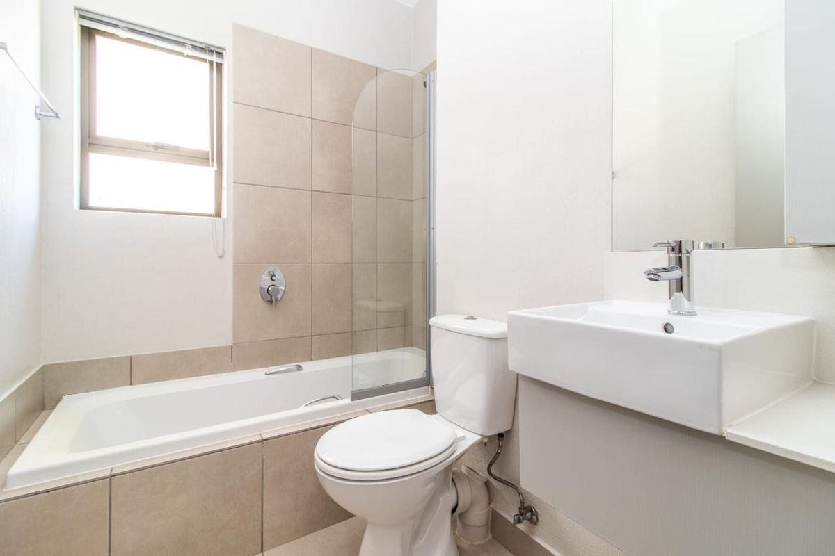 A clean, modern bathroom featuring a bathtub with a glass shower screen, a wall-mounted vanity basin, and neutral wall tiling.