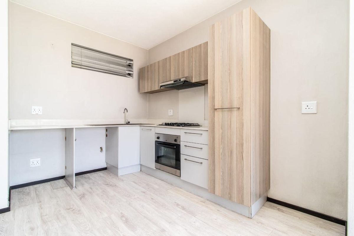 A compact kitchen featuring light wood-tone cabinetry, built-in oven, gas hob, and laminate flooring, offering a functional space ready for personalization.