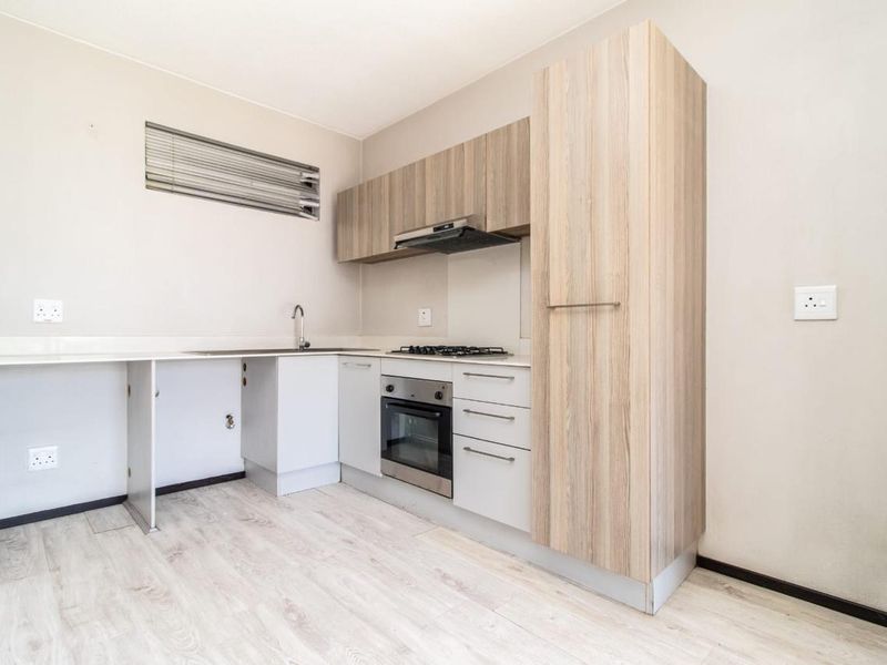 A compact kitchen featuring light wood-tone cabinetry, built-in oven, gas hob, and laminate flooring, offering a functional space ready for personalization.