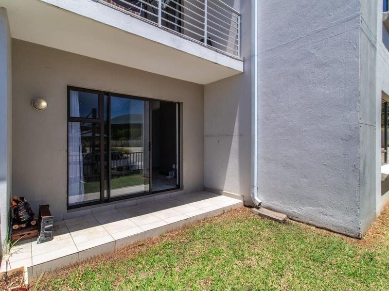 A ground floor tiled patio area featuring a sliding glass door entrance and an overhead balcony with metal railings.