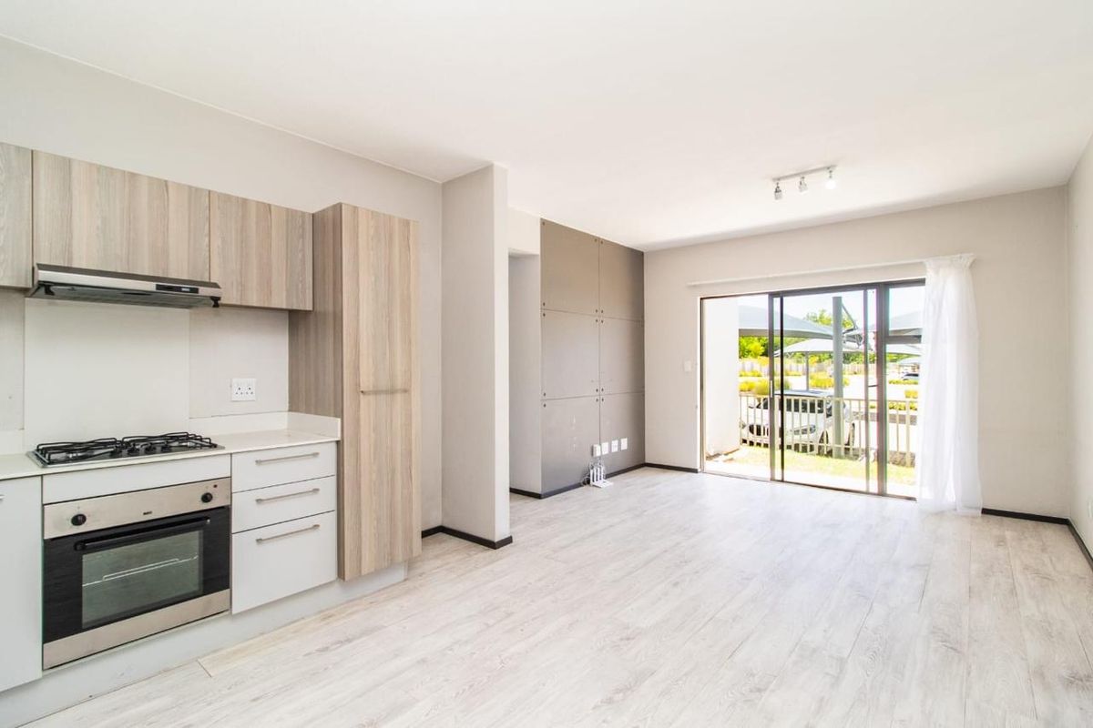 Modern open-plan kitchen and living area featuring light wood-finish cabinetry, built-in appliances, and sliding glass doors leading to an outdoor space.