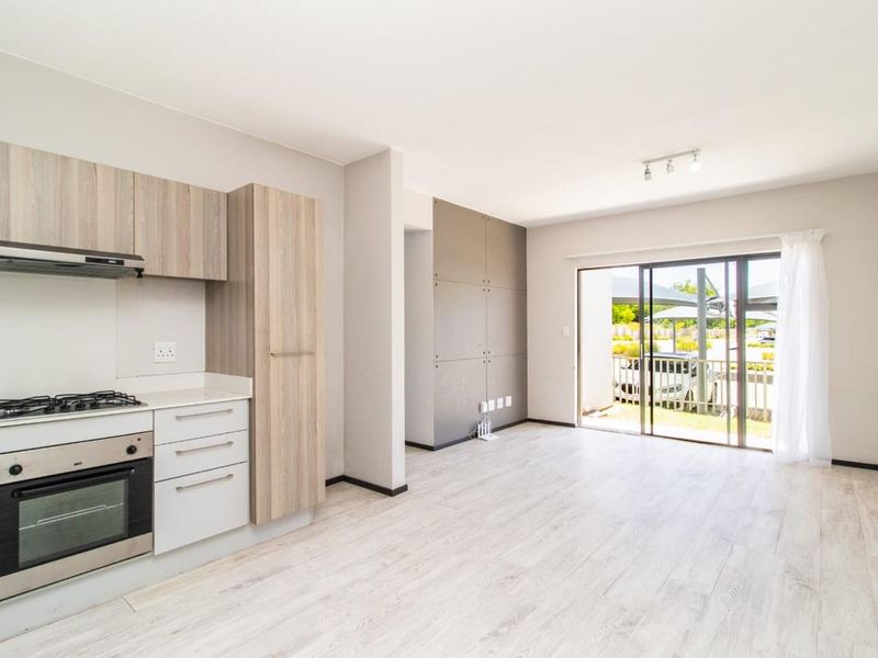 Modern open-plan kitchen and living area featuring light wood-finish cabinetry, built-in appliances, and sliding glass doors leading to an outdoor space.