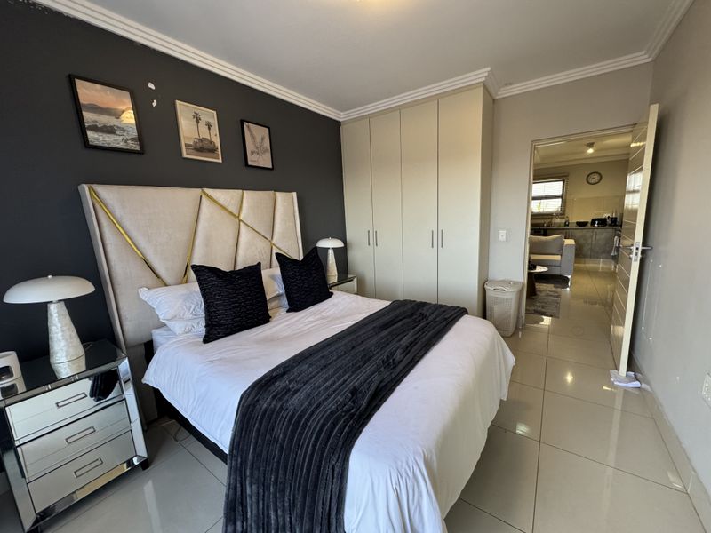 A well-maintained bedroom featuring built-in cupboards, tiled flooring, and decorative cornicing, with an adjoining view into the living area.