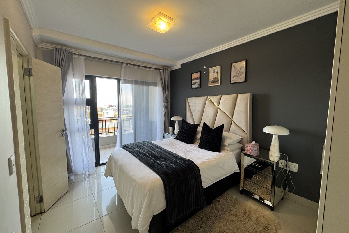 A well-maintained bedroom featuring tiled floors, a dark accent wall, and direct access to a private balcony through sliding glass doors.