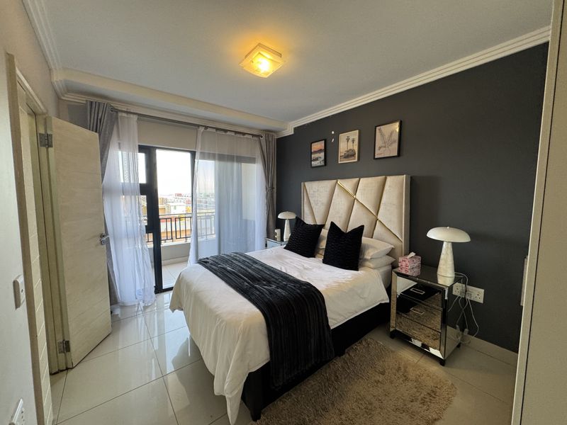 A well-maintained bedroom featuring tiled floors, a dark accent wall, and direct access to a private balcony through sliding glass doors.