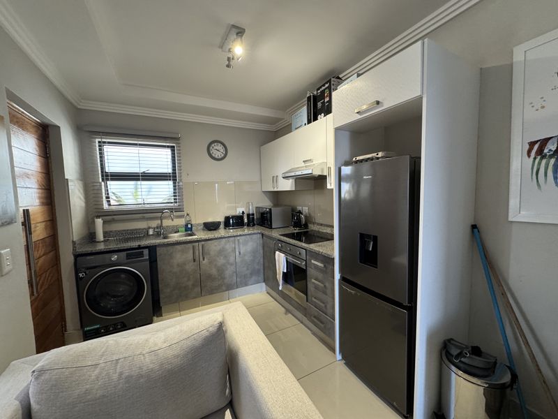 A compact, modern kitchen featuring granite countertops, built-in cabinetry, integrated oven and hob, and tiled flooring, efficiently designed for apartment living.