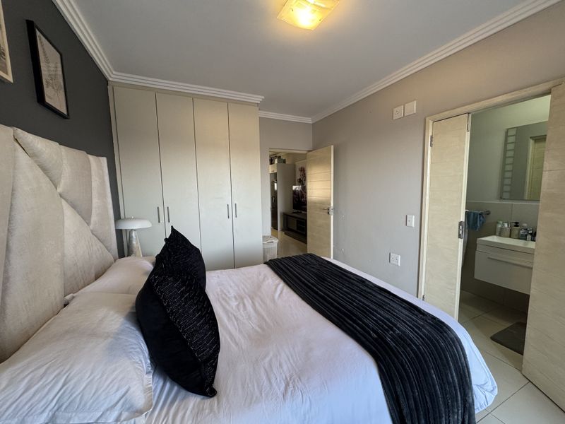 A well-maintained bedroom featuring built-in cupboards, crown molding, and direct access to an en-suite bathroom with a modern vanity.