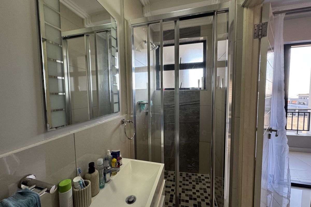 A functional bathroom featuring a shower enclosure with tiled accents, a vanity basin, and a wall-mounted mirror.