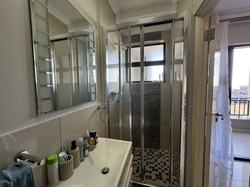 A functional bathroom featuring a shower enclosure with tiled accents, a vanity basin, and a wall-mounted mirror.
