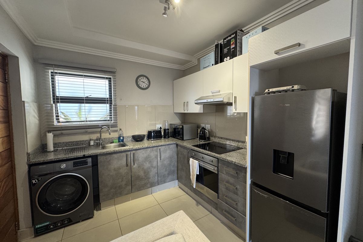 A functional kitchen featuring granite countertops, built-in cabinetry, integrated oven and hob, and tiled flooring with a dedicated space for a washing machine.
