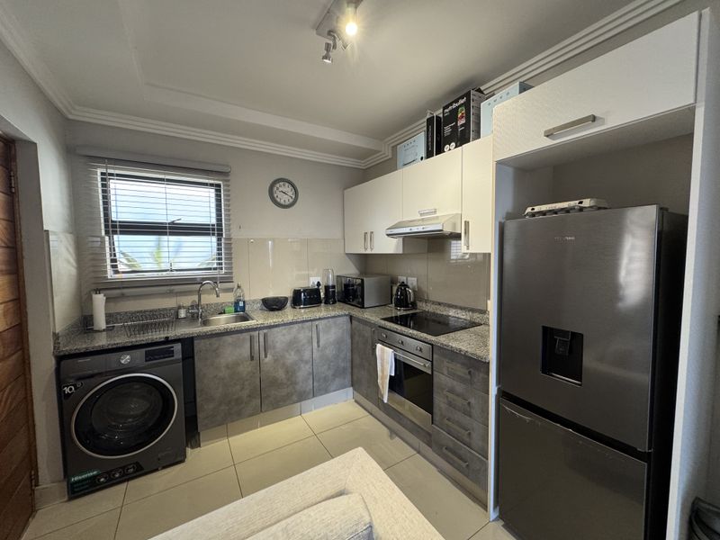 A functional kitchen featuring granite countertops, built-in cabinetry, integrated oven and hob, and tiled flooring with a dedicated space for a washing machine.