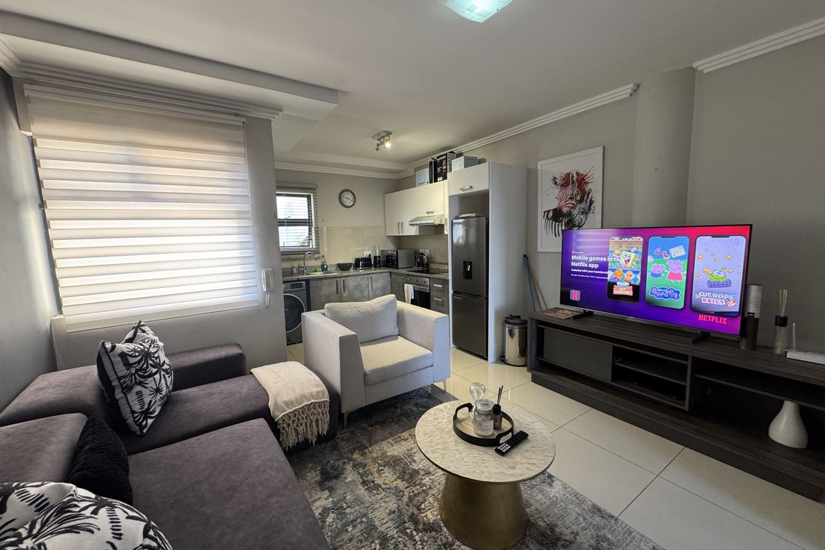 An open-plan living area featuring a compact kitchen with built-in cabinetry, granite countertops, and tiled flooring, seamlessly connected to the lounge space.