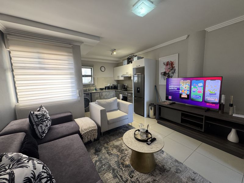 An open-plan living area featuring a compact kitchen with built-in cabinetry, granite countertops, and tiled flooring, seamlessly connected to the lounge space.