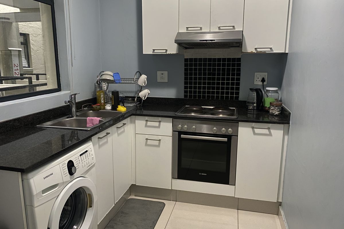 Compact kitchen featuring white cabinetry, granite countertops, built-in oven, electric hob, extractor fan, and integrated laundry plumbing.