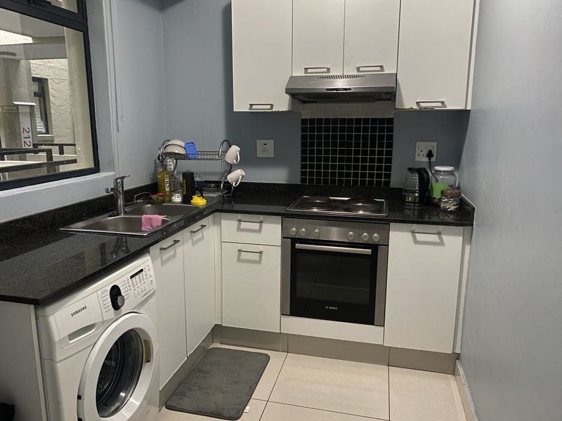 Compact kitchen featuring white cabinetry, granite countertops, built-in oven, electric hob, extractor fan, and integrated laundry plumbing.