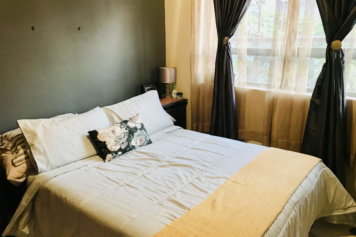 A cozy bedroom featuring a dark accent wall and large window with curtains, providing natural light and a comfortable living space.