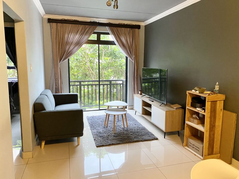 A well-lit living room featuring large sliding glass doors leading to a balcony, tiled flooring, and a modern accent wall.