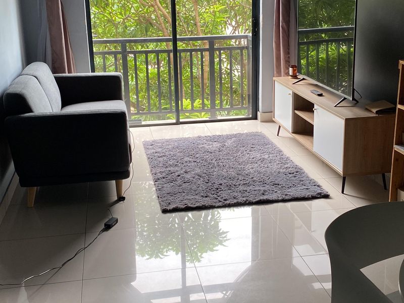 A living room featuring large format floor tiles, dark accent walls, and a sliding glass door leading to a balcony with greenery views.