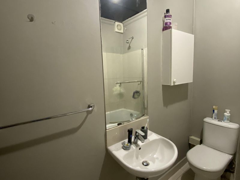 A functional bathroom featuring a wall-mounted basin, toilet, and shower area with tiled flooring and neutral wall finishes.