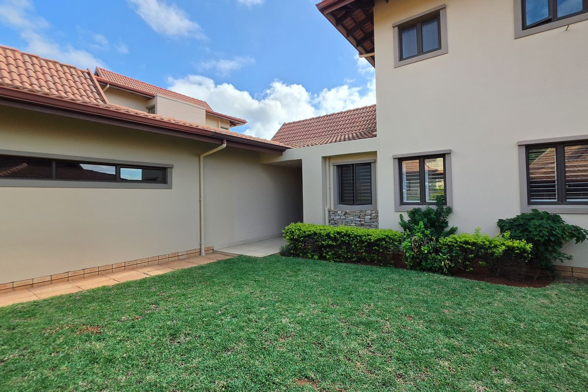Rear view of the townhouse featuring a well-maintained lawn, plastered exterior walls, tiled roofing, and modern aluminium window frames.