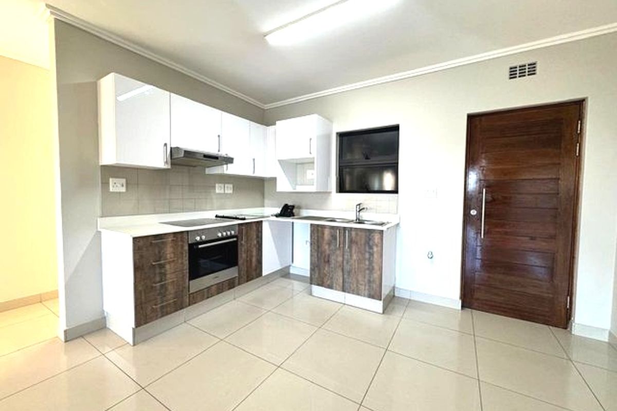 Modern kitchen featuring two-tone cabinetry, built-in oven and hob, extractor fan, stainless steel sink, and neutral tiled flooring.
