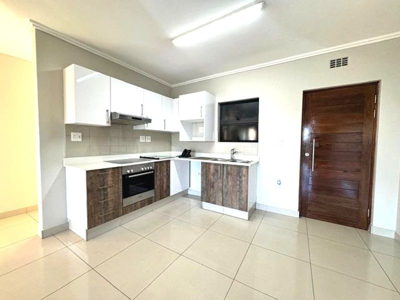 Modern kitchen featuring two-tone cabinetry, built-in oven and hob, extractor fan, stainless steel sink, and neutral tiled flooring.