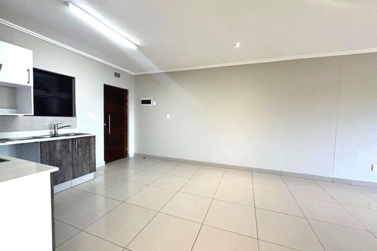 An open-plan living area featuring tiled flooring, neutral walls, and a modern kitchen corner with built-in cabinetry and a stainless steel sink.