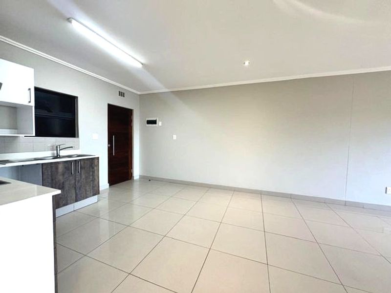 An open-plan living area featuring tiled flooring, neutral walls, and a modern kitchen corner with built-in cabinetry and a stainless steel sink.
