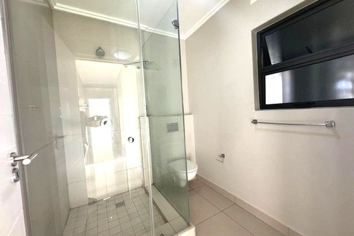 A clean, modern bathroom featuring a glass-enclosed shower, wall-mounted toilet, and neutral tiled finishes throughout.
