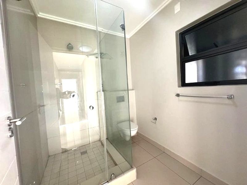 A clean, modern bathroom featuring a glass-enclosed shower, wall-mounted toilet, and neutral tiled finishes throughout.