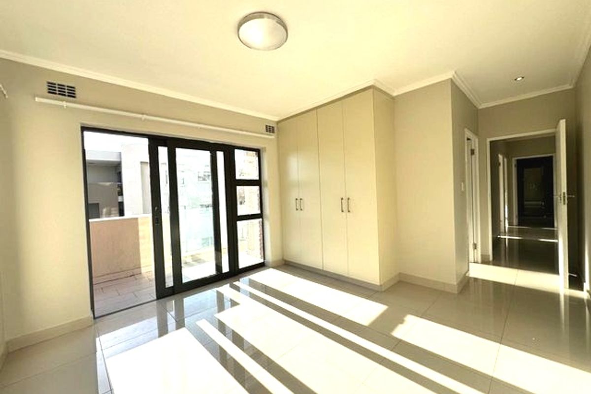 A bright, empty bedroom featuring tiled flooring, built-in cupboards, and a sliding glass door providing access to an outdoor balcony area.