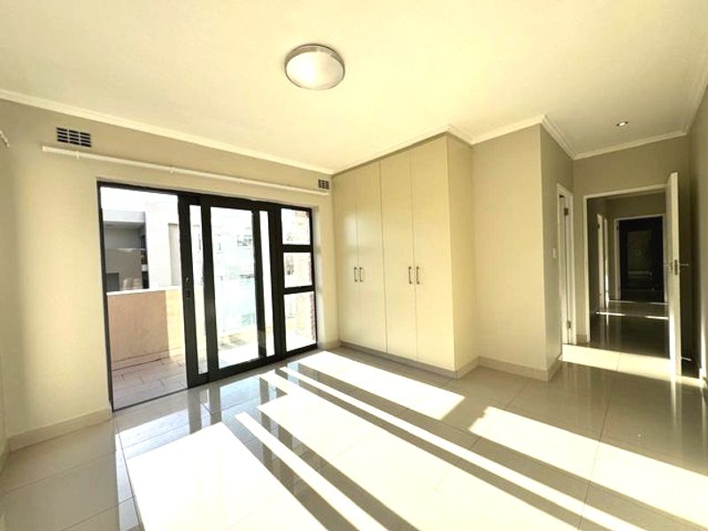 A bright, empty bedroom featuring tiled flooring, built-in cupboards, and a sliding glass door providing access to an outdoor balcony area.