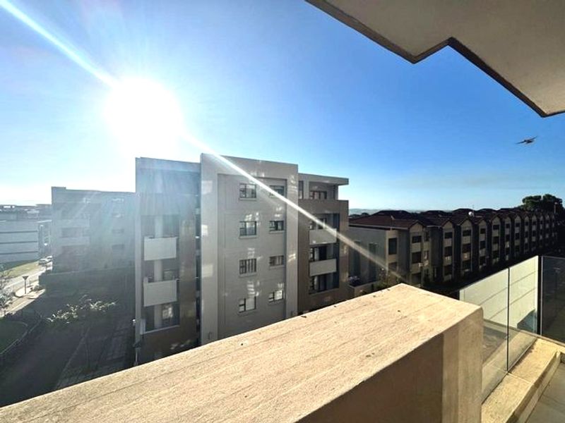 A modern apartment balcony featuring a glass balustrade and concrete parapet, offering an elevated view of the surrounding residential complex.