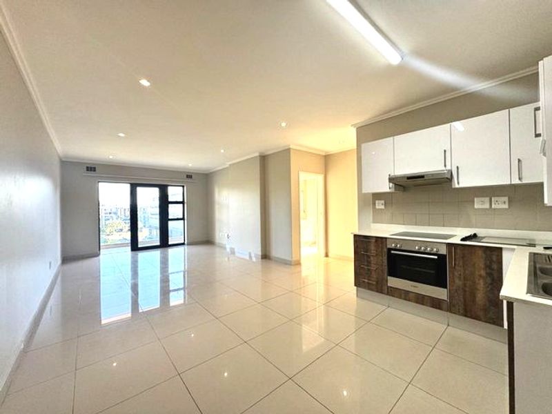 Spacious open-plan living area featuring a modern kitchen with built-in appliances, sleek cabinetry, and large sliding doors leading to a balcony.