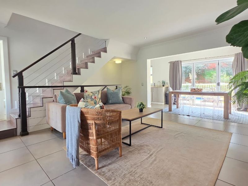 Spacious open-plan living and dining area featuring tiled floors, a modern staircase with metal balustrades, and sliding glass doors leading to the outdoor space.