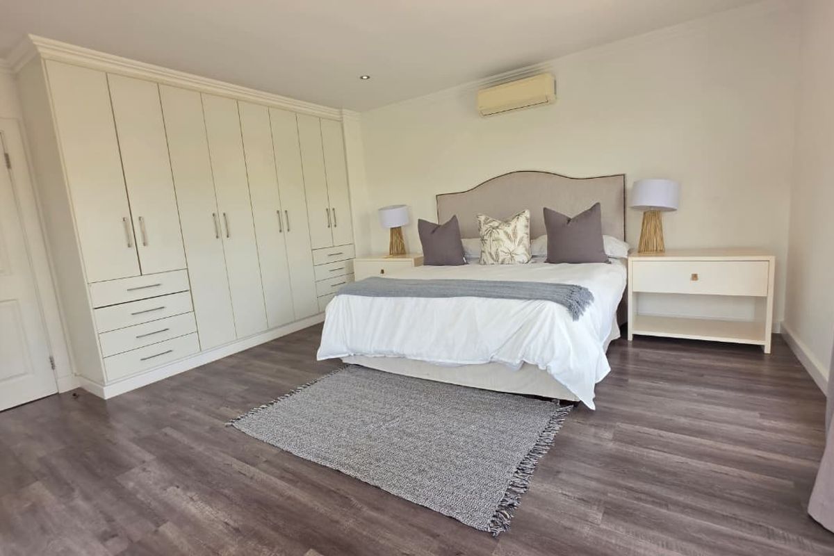 Spacious bedroom featuring extensive built-in cabinetry, modern laminate flooring, and a wall-mounted air conditioning unit for climate control.