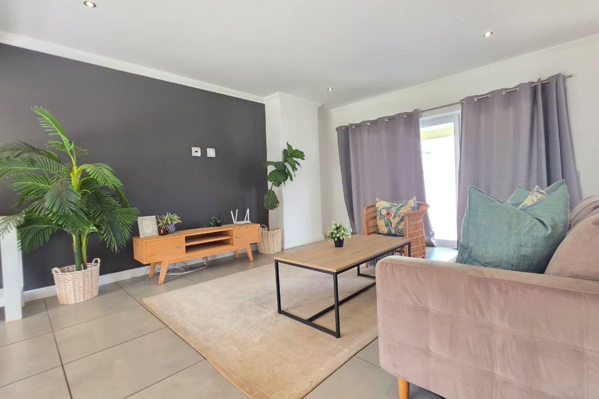 A bright and modern living room featuring large format floor tiles, a dark accent wall, and direct access to the outdoor area via a sliding door.