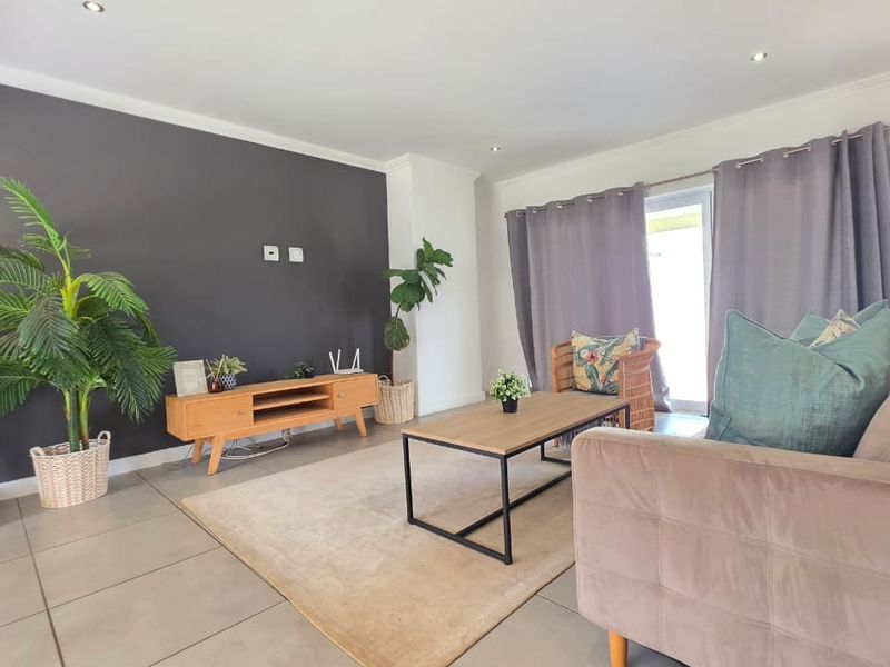 A bright and modern living room featuring large format floor tiles, a dark accent wall, and direct access to the outdoor area via a sliding door.