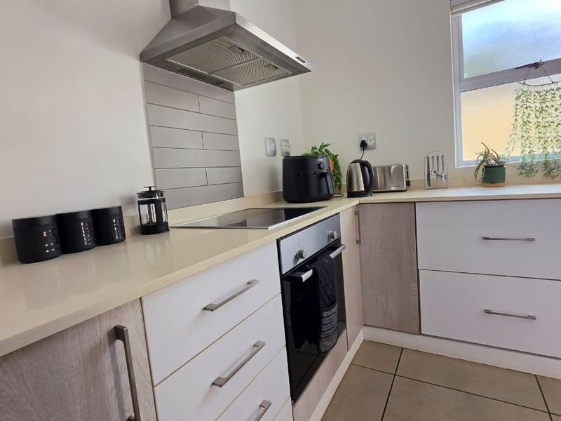 Modern kitchen featuring built-in oven, electric hob, stainless steel extractor fan, stone countertops, and ample cabinetry with tiled flooring.