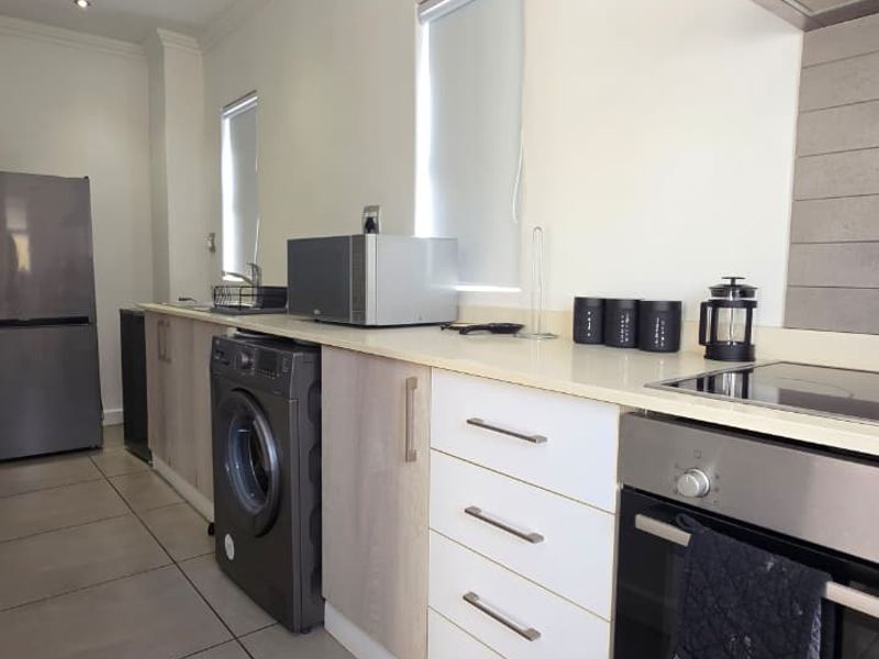 Modern kitchen featuring sleek cabinetry, stone countertops, built-in oven, electric hob, extractor fan, and large format floor tiles.