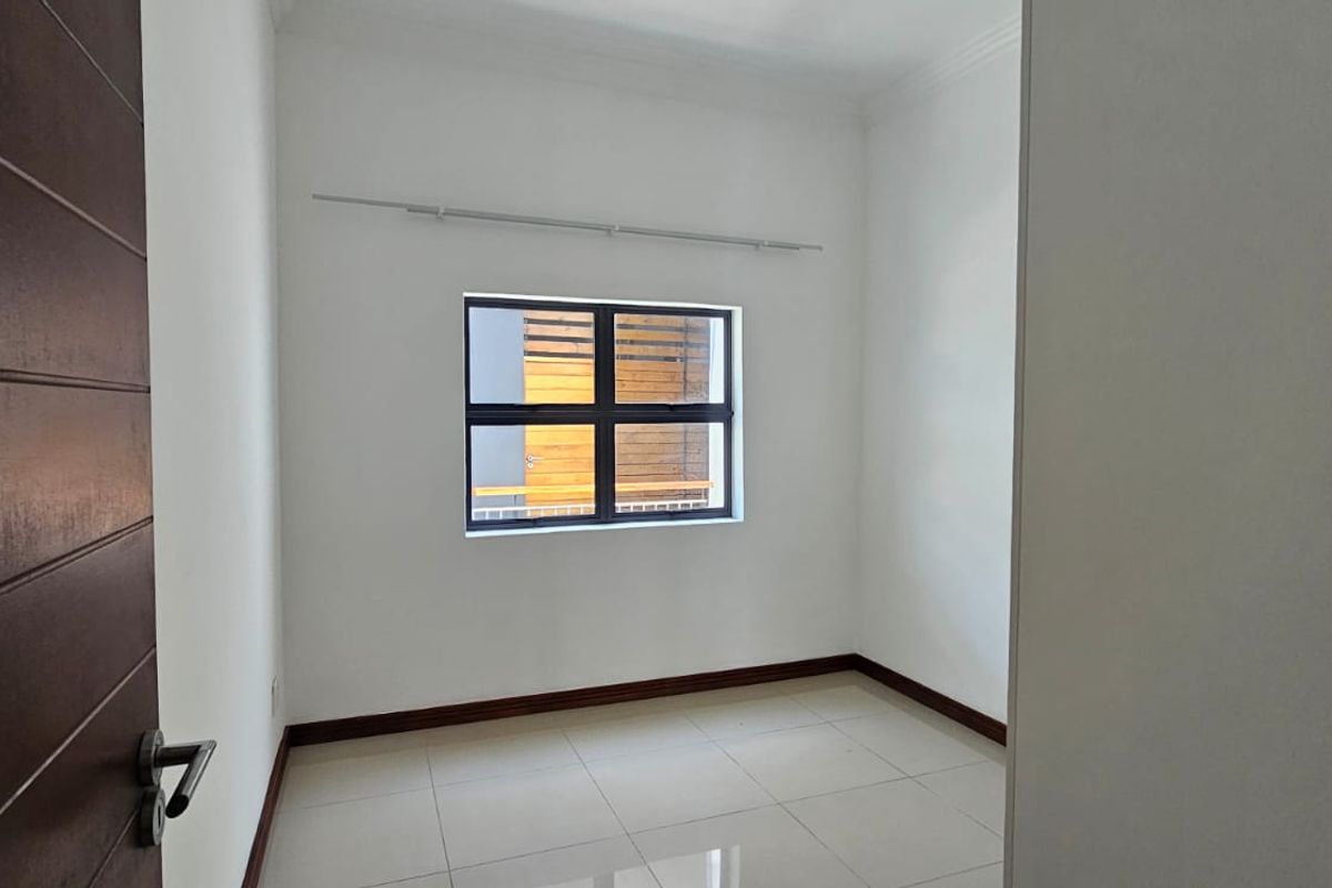 A clean, empty bedroom featuring neutral tiled flooring, white walls, and an aluminium-framed window with a fitted curtain rail.